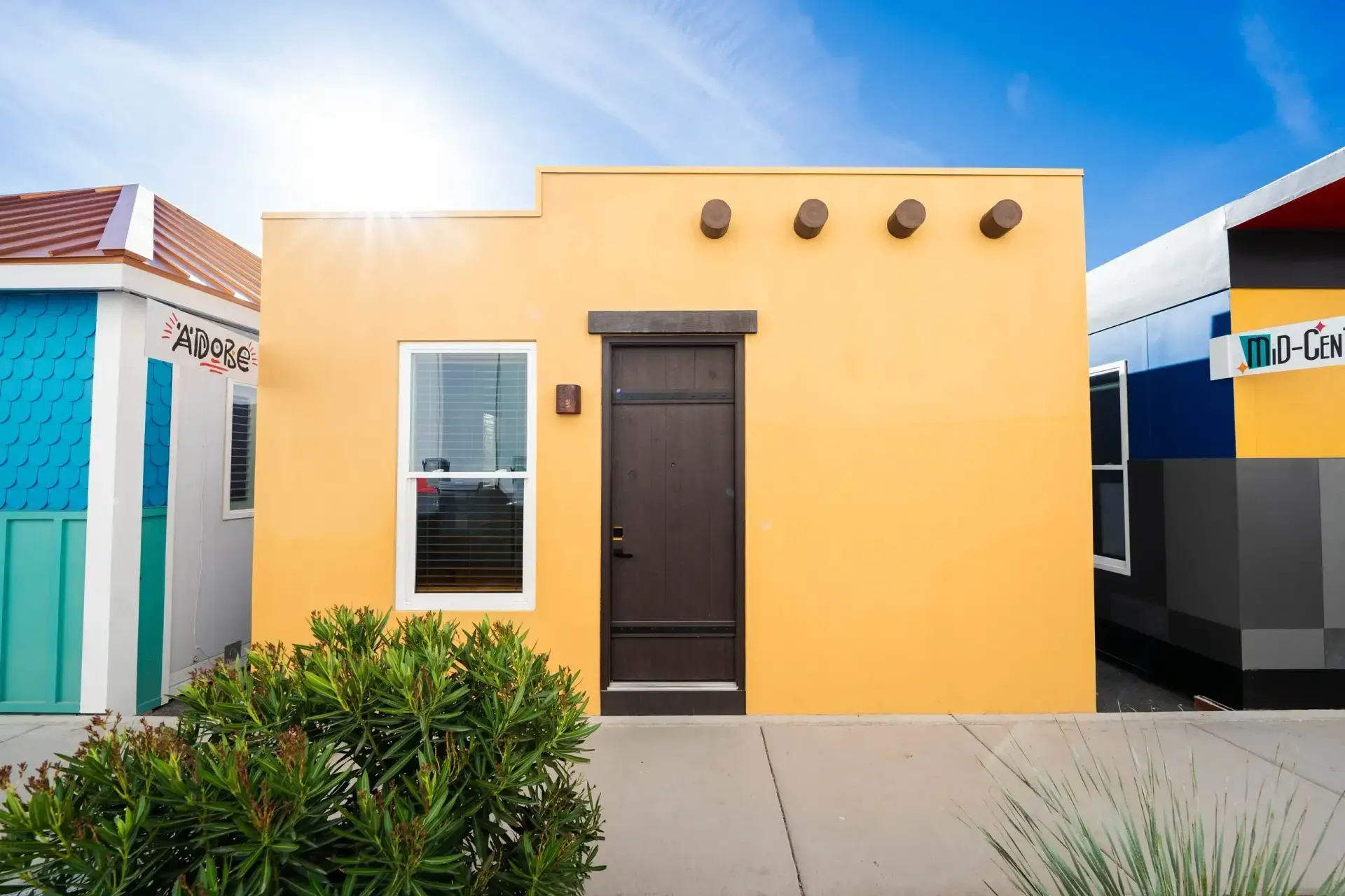 Modern Boxabl modular home exterior in San Diego, featuring a sleek yellow facade, a brown front door, and a window, surrounded by greenery, showcasing innovative design and efficient living.