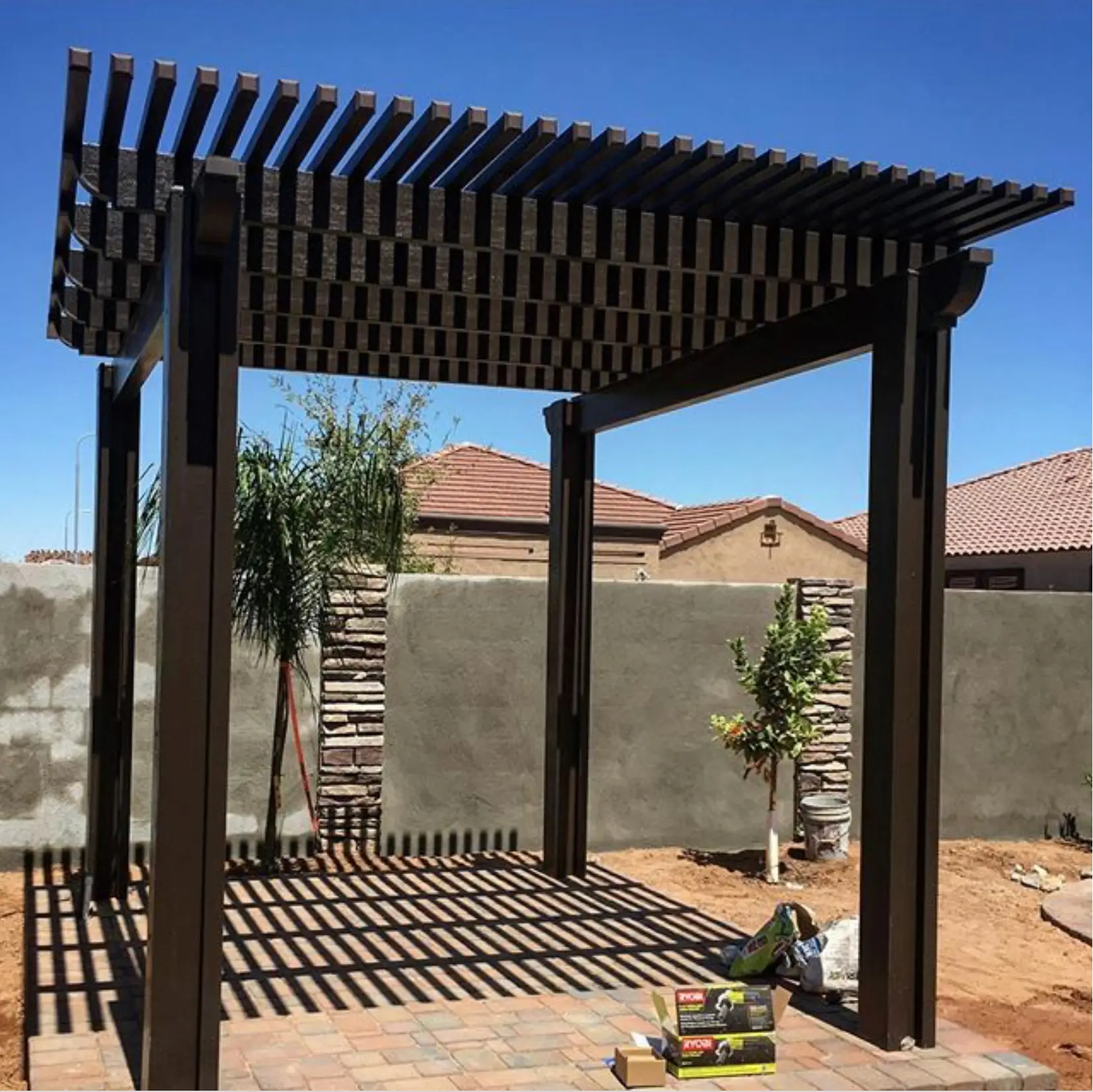Custom louvered pergola providing shade in a backyard, featuring a modern design, surrounded by landscaping elements and a clear blue sky, highlighting outdoor living potential in San Diego.