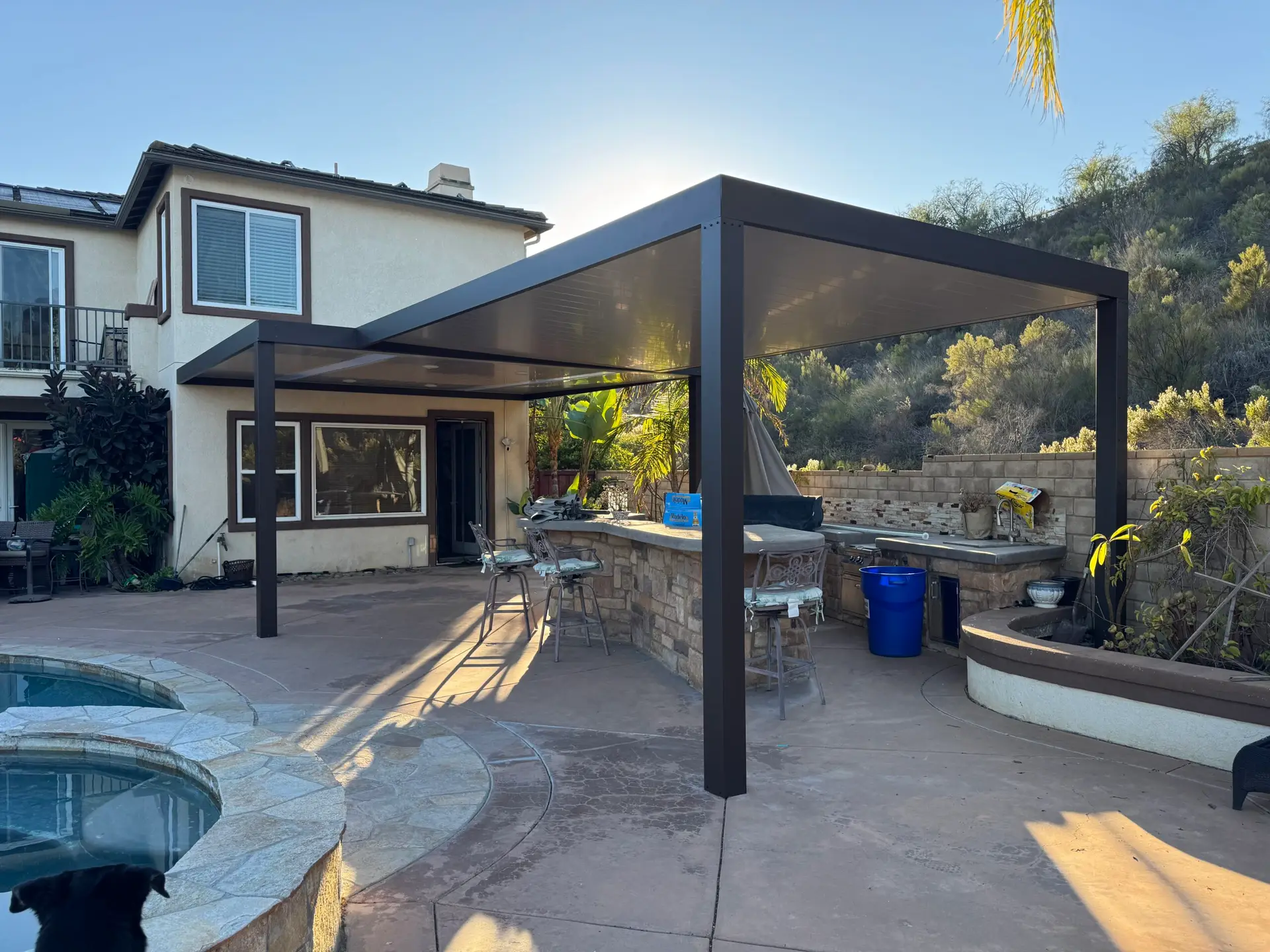 Modern aluminum patio cover in a San Diego backyard, providing shade over a stone outdoor kitchen and seating area, enhancing outdoor living space.