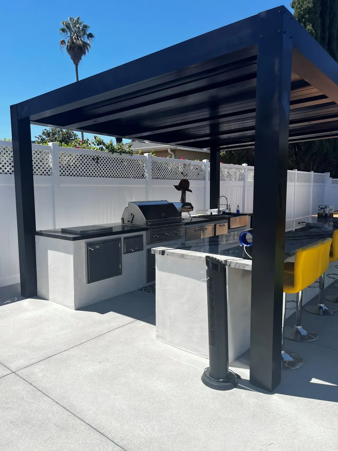 Custom louvered pergola with outdoor kitchen featuring stainless steel grill, sleek countertops, and bar seating in sunny San Diego backyard.