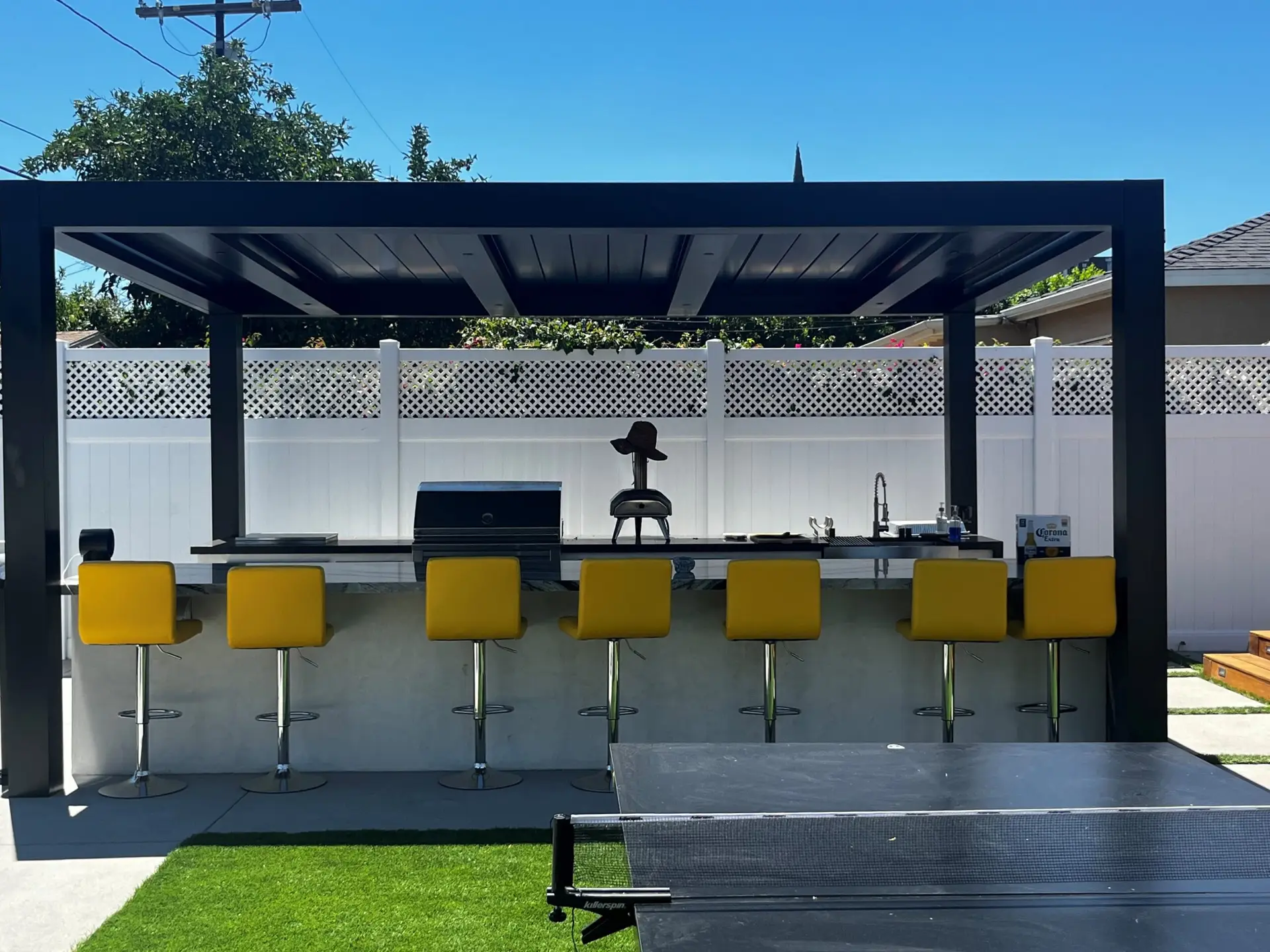 Custom-designed pergola with modern outdoor bar featuring yellow stools, grill, and countertop, enhancing outdoor living space in San Diego backyard.