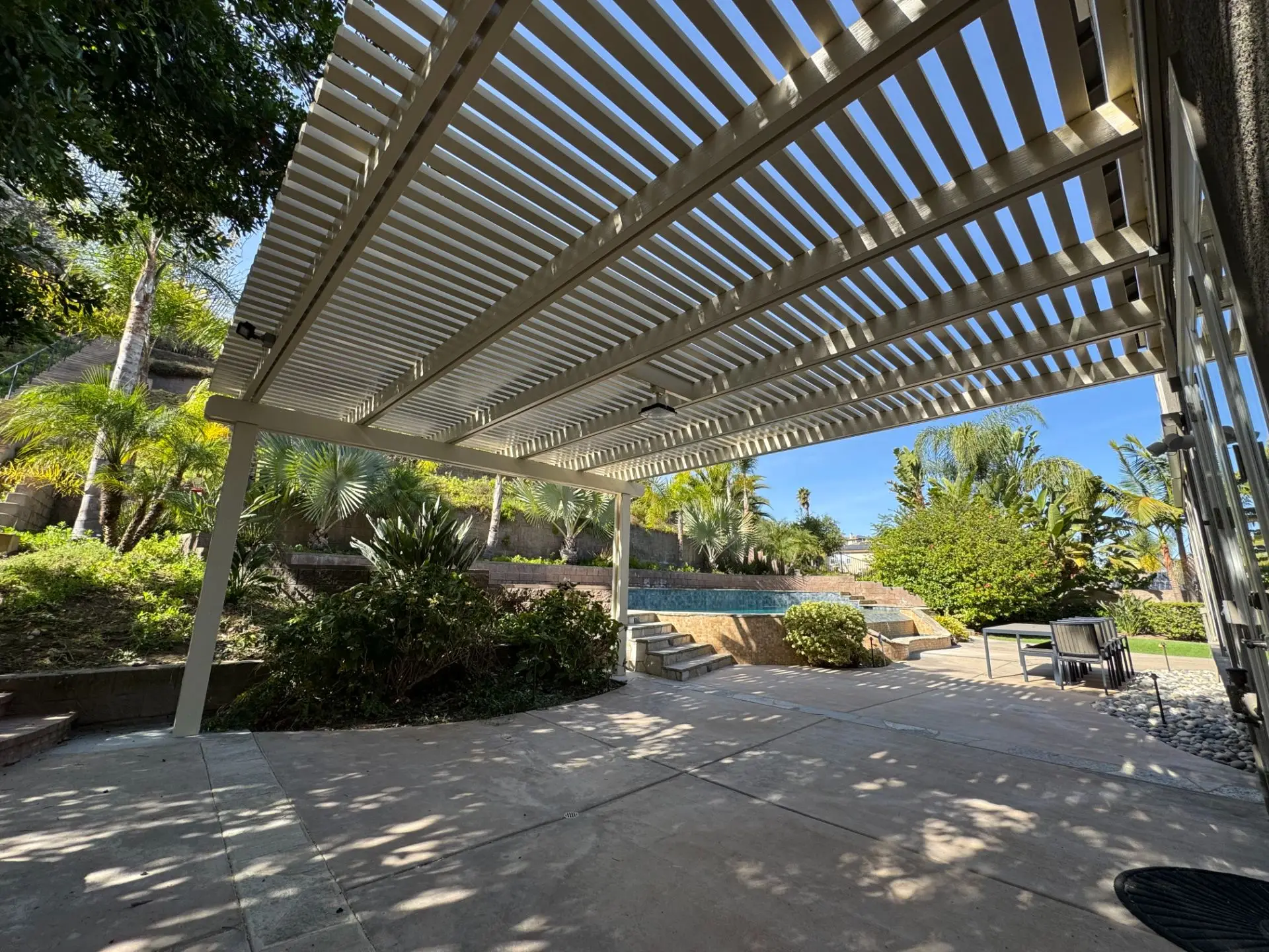 Aluminum pergola installation enhancing a stylish outdoor living space with lush landscaping and a pool in Poway, CA.