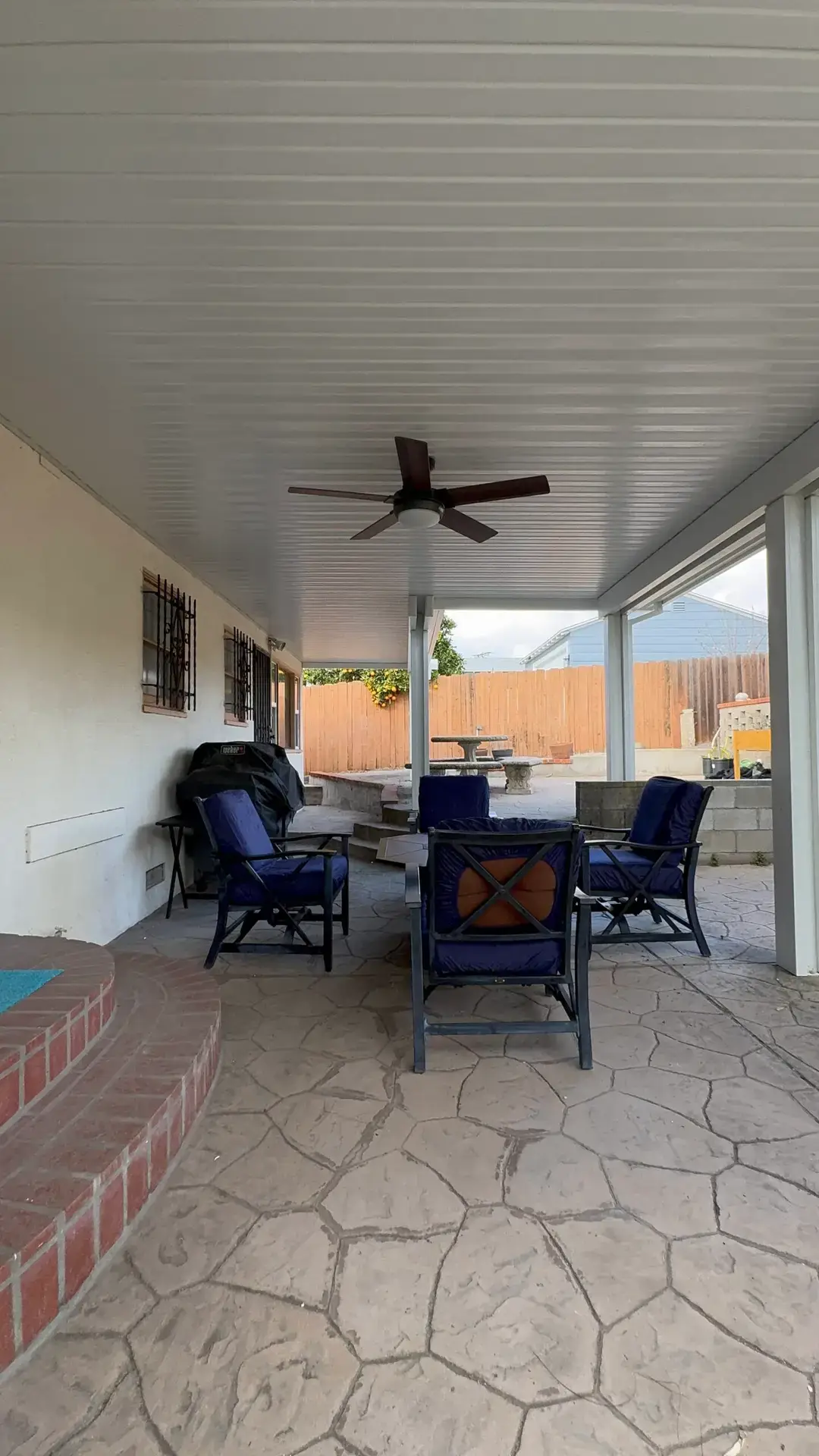 Residential patio cover installation featuring a modern Elitewood aluminum cover, outdoor seating area with blue chairs, and a ceiling fan, in La Mesa, CA.