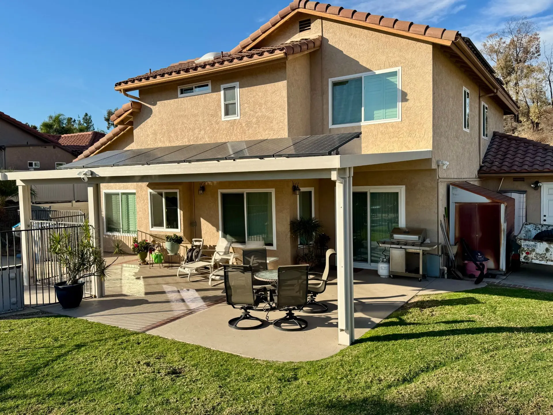 Residential solar-ready aluminum patio cover installation in Rancho San Diego, featuring a stylish outdoor seating area, solar panels on the roof, and lush green grass.