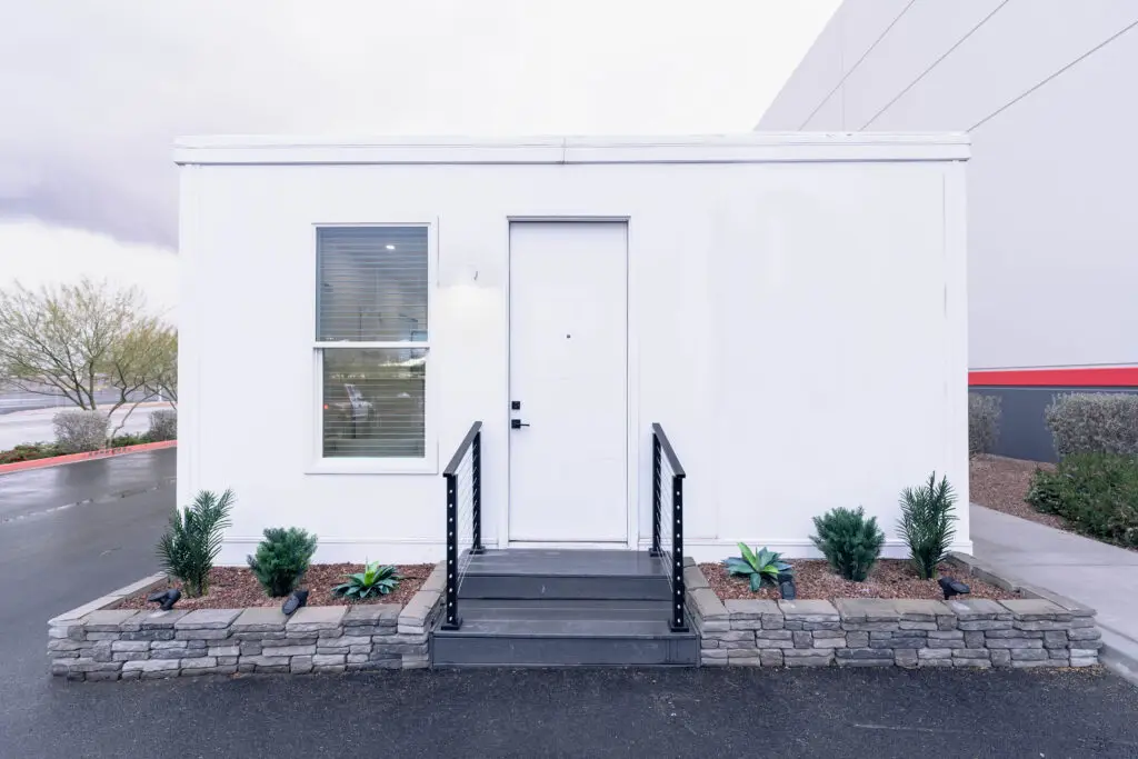 Modular Boxabl home with modern design, featuring a white exterior, large windows, and a welcoming entrance, surrounded by minimal landscaping, emphasizing affordability and innovative construction methods for San Diego living.