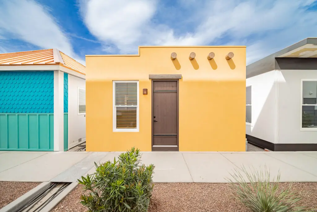 Modular Boxabl home with a yellow exterior and modern design, showcasing earthquake-resistant features, surrounded by other colorful units in a San Diego neighborhood.