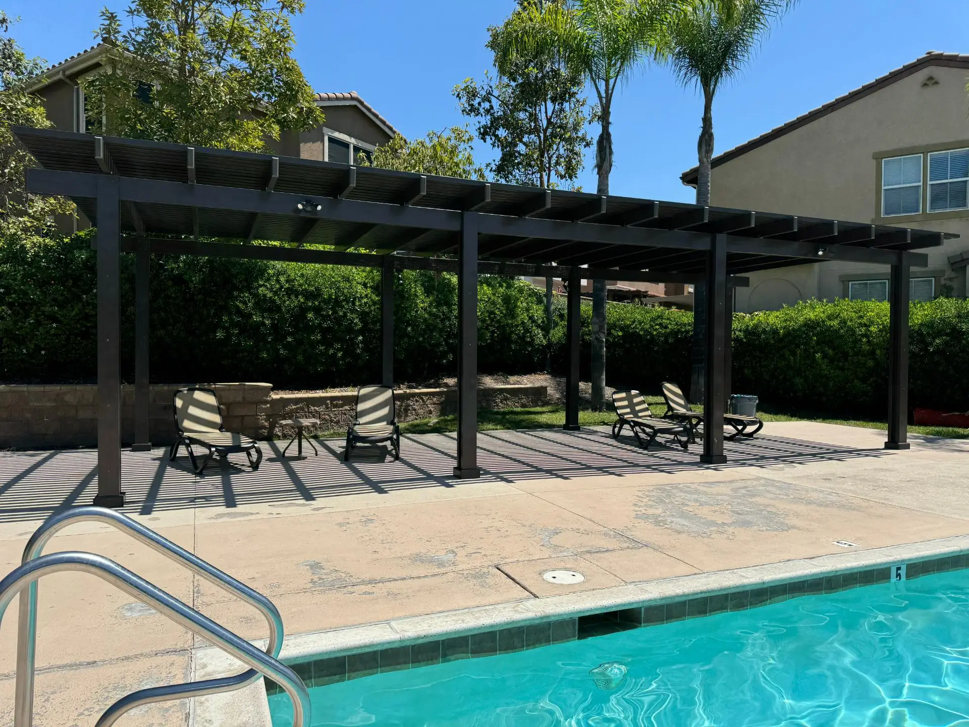 Custom insulated aluminum patio cover with integrated LED lights and ceiling fans, featuring lounge chairs and a table in a landscaped backyard setting, enhancing outdoor living space.